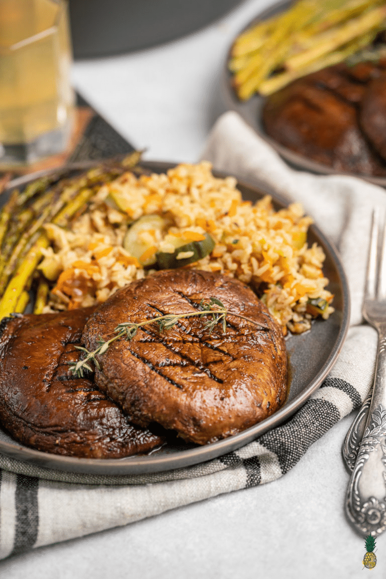 Grilled portobello mushrooms with a side of additional vegetables on a grey plate. 