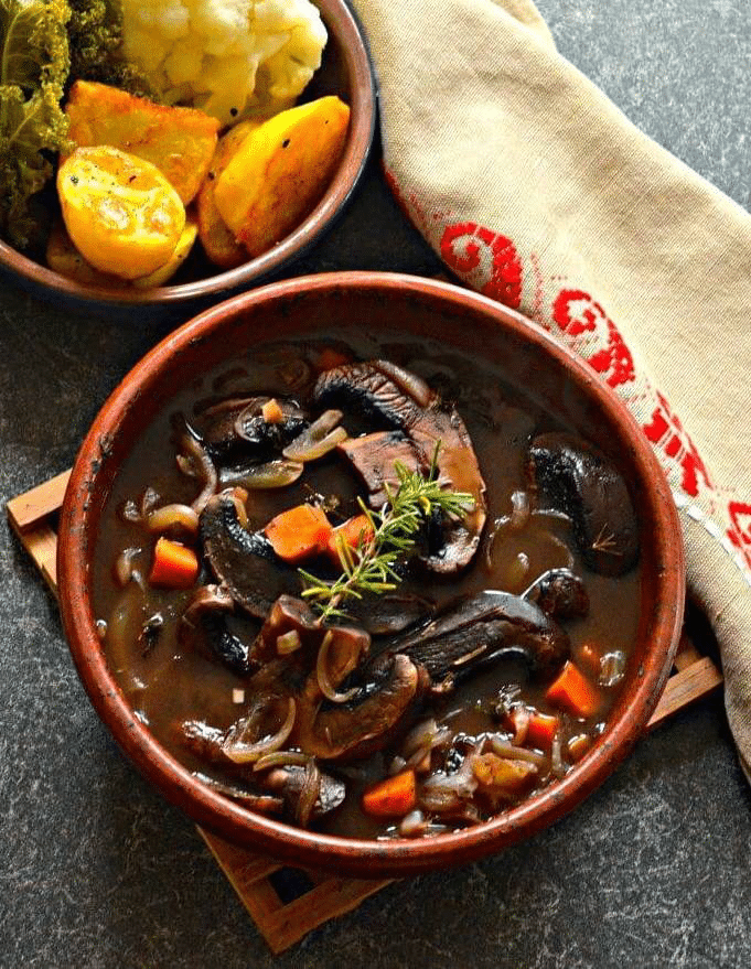 Hearty soup in a brown bowl garnished with fresh herbs. 