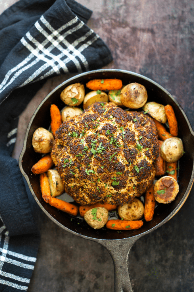 birds eye view of Roasted cauliflower with carrots and potatoes garnished with fresh herbs in a cast iron skillet.