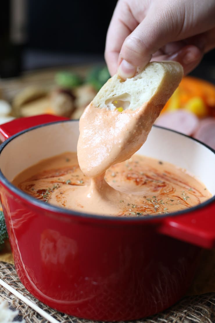 close up of bread being dipped into gluten free pizza fondue from a red pot