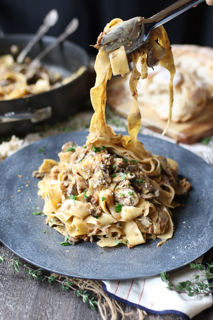 Fork taking a bite out of pasta dish on a grey plate garnished with herbs.