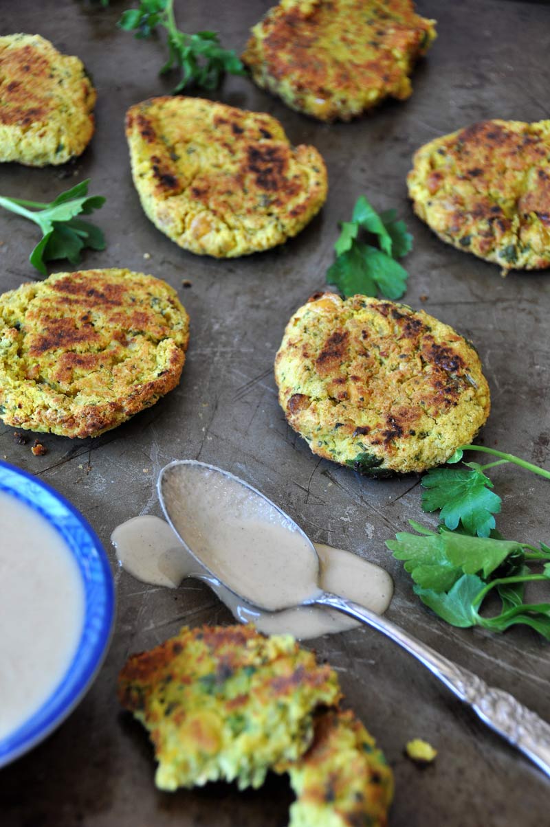 Scattered falafel and parsley on a metal surface with a spoon of sauce. 