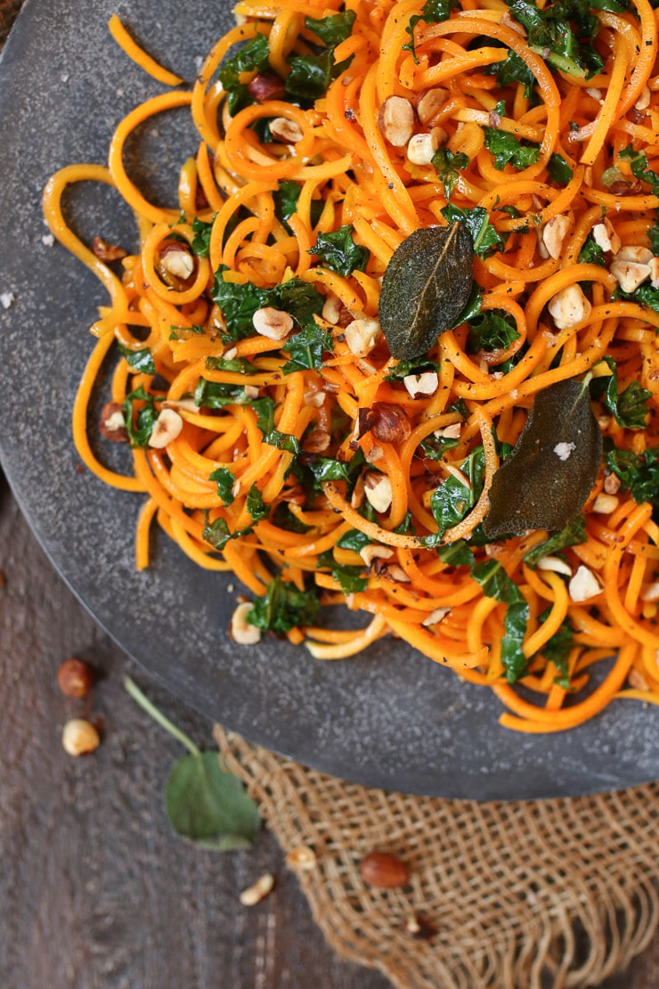 Close up of squash zoodles topped with fried sage leaves and chopped hazelnuts.