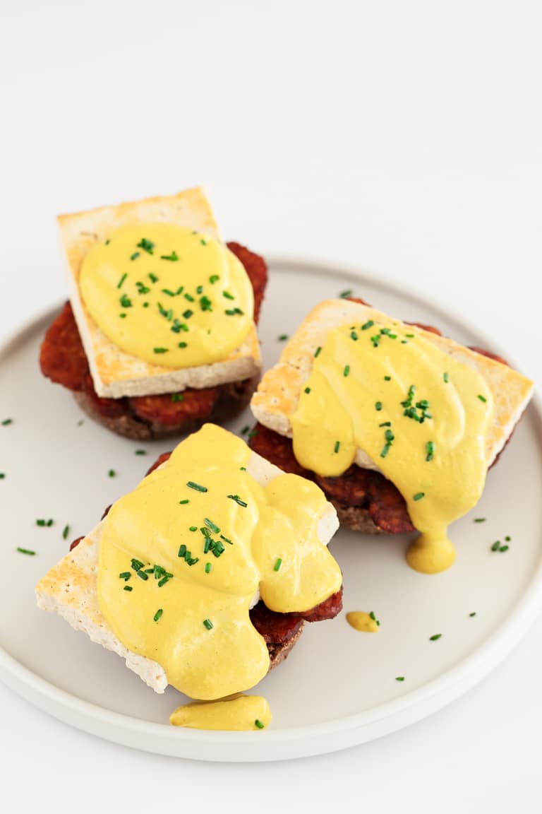 Three vegan eggs benedicts on a white plate.