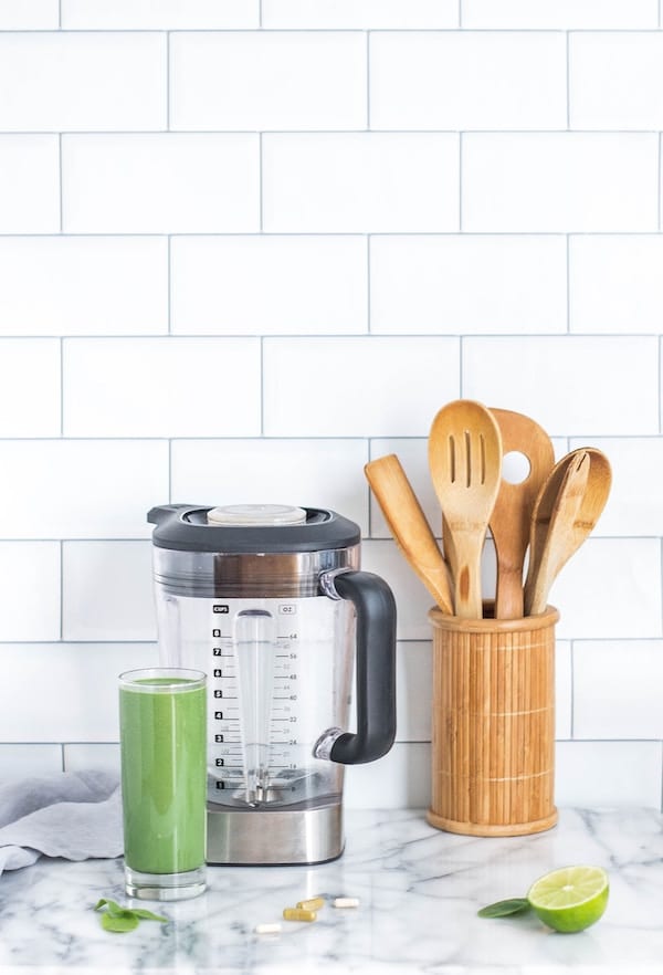 Kitchen utensils in a vase next to a green smoothie and blender.