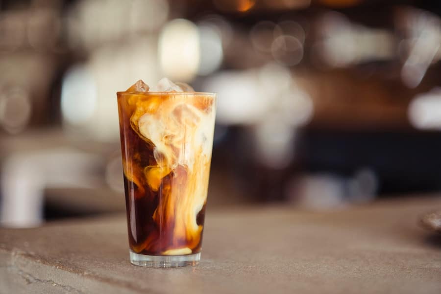 Tall clear glass containing coffee with milk.