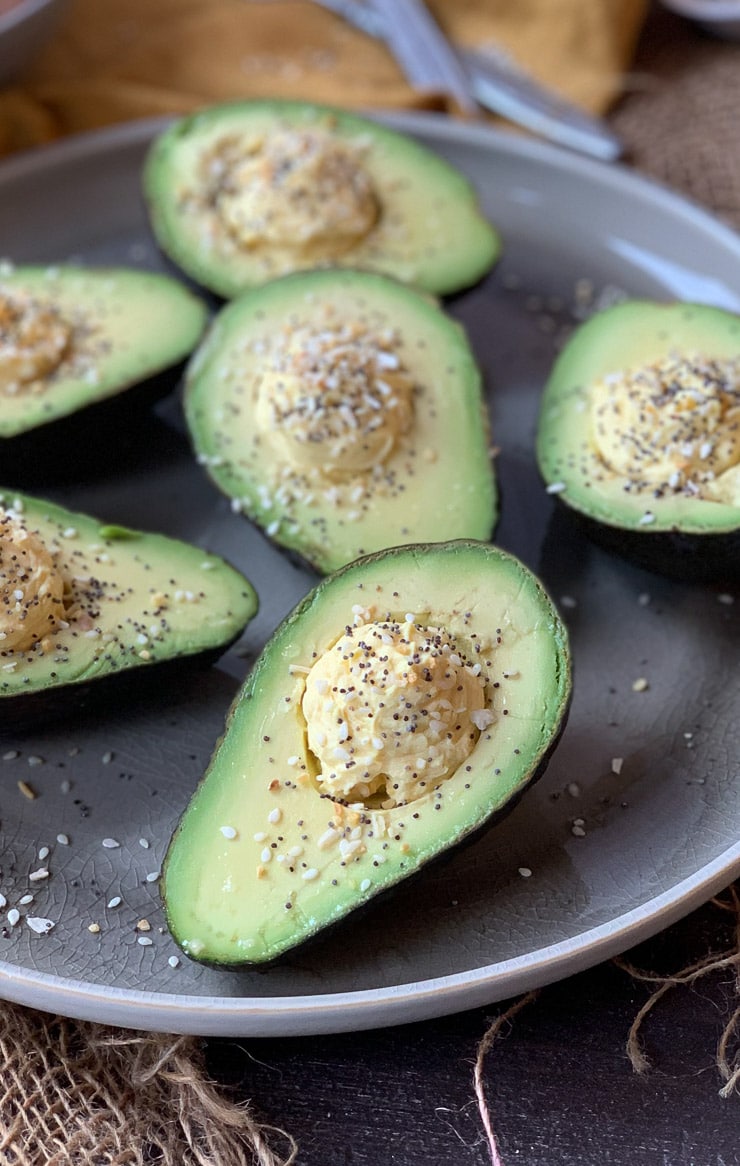 Full shot of multiple avocado devilled eggs topped with everything bagel spice on a large grey circular plate.