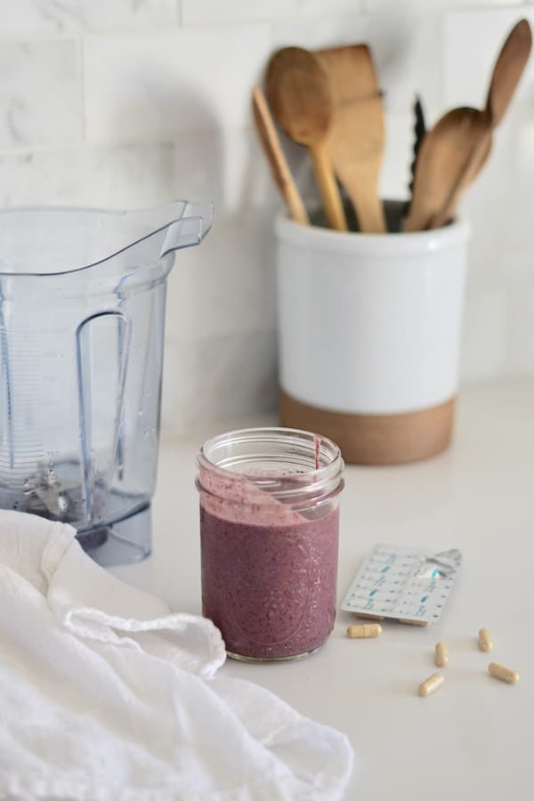 Purple smoothie in a clear mason jar next to a blender.