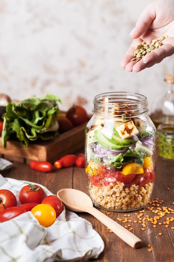 Mason jar layered salad being topped with seeds.