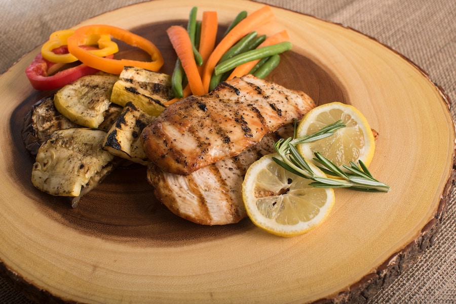 Grilled chicken and vegetables on a wooden plate.