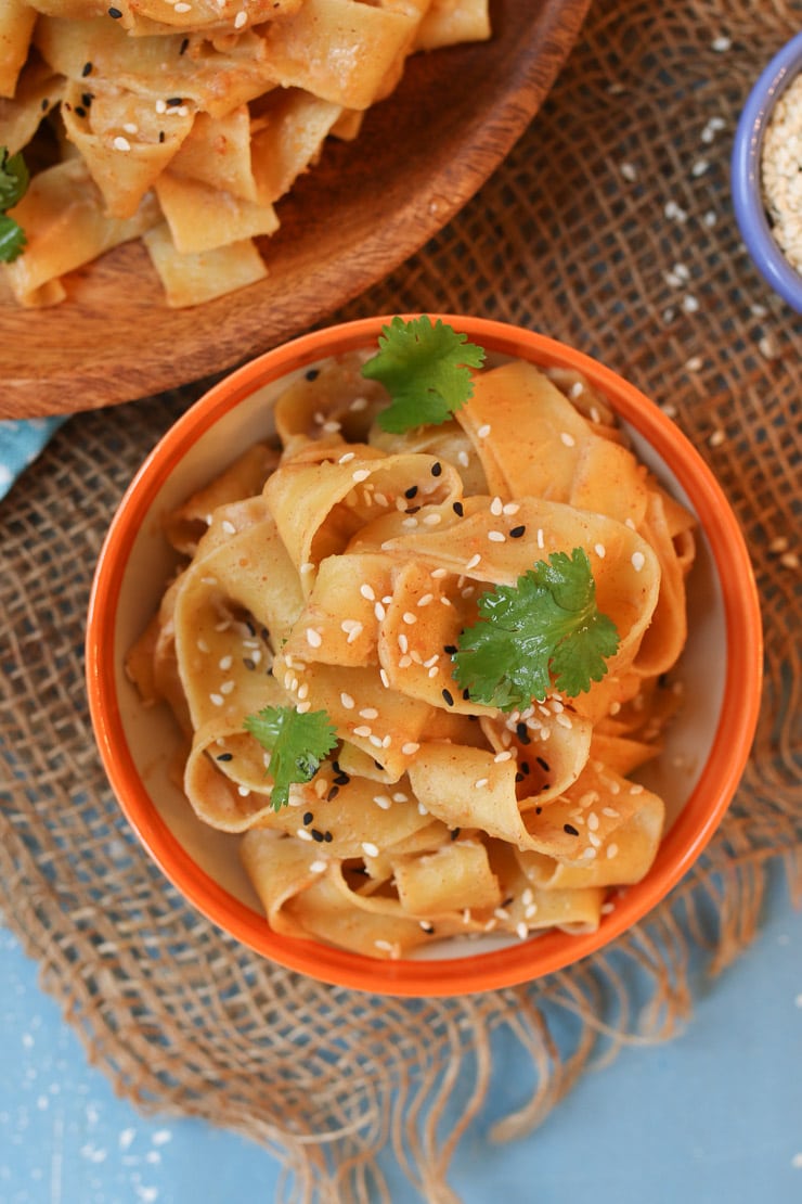 Peanut butter sesame noodles in an orange bowl topped with sesame seed and cilantro