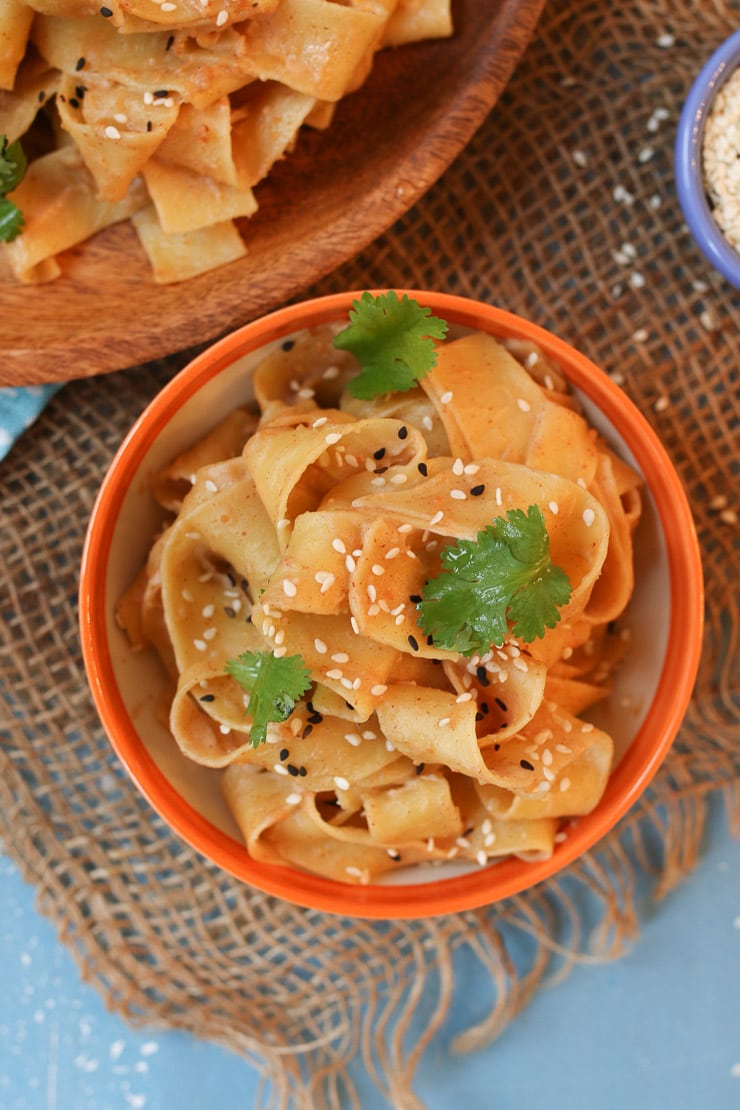 Peanut butter sesame noodles in an orange bowl topped with sesame seed and cilantro 