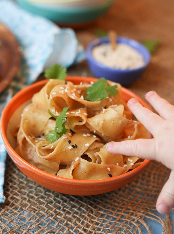 Baby's hand reaching out to grab a peanut butter sesame noodle. 