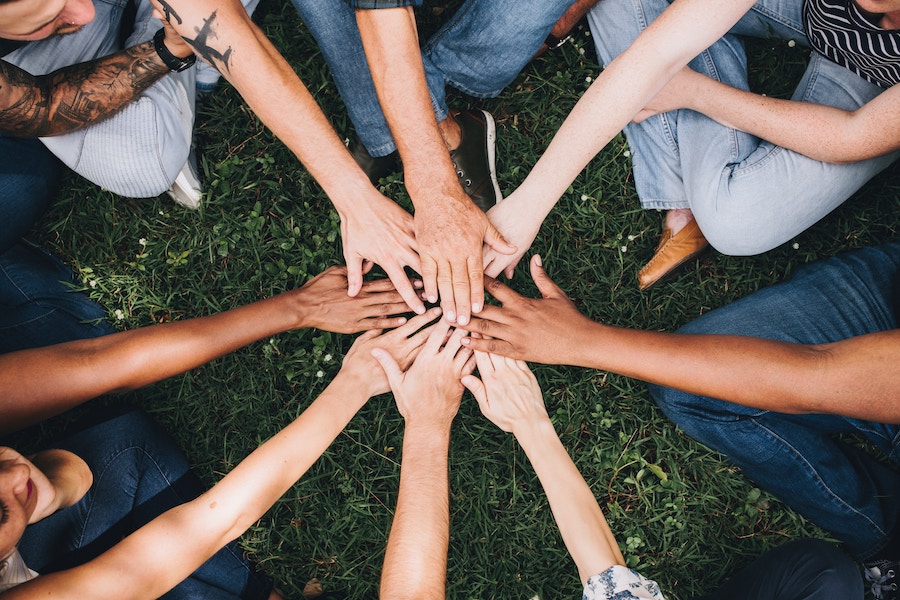 Birds eye view of multiple hands joining together with a grass background.