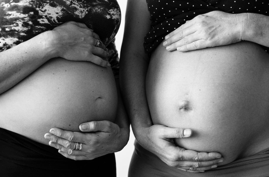 Black and white photo of two people holding their pregnant stomachs.