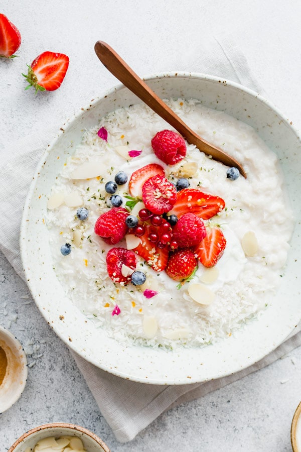 A large white bowl with coconut rice pudding, topped with strawberries and raspberries. 