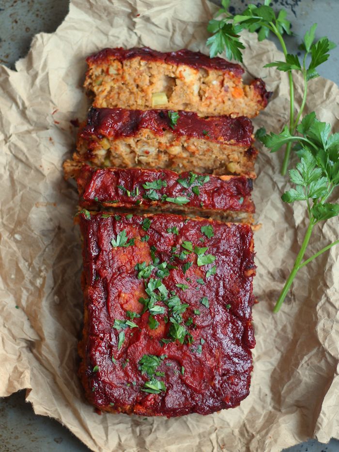 A birds eye view of a meat loaf with a few slices cut on brown paper and garnished with parsley.