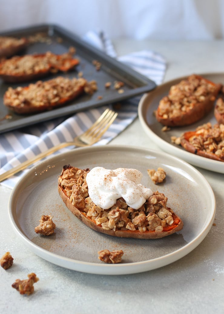 A stuffed sweet potato with vegan apple crisp on a grey plate topped with vegan cream.