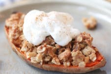 Close up of sweet potato stuffed with apple crisp topped with a vegan cream on a grey plate.