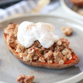 Close up of sweet potato stuffed with apple crisp topped with a vegan cream on a grey plate.