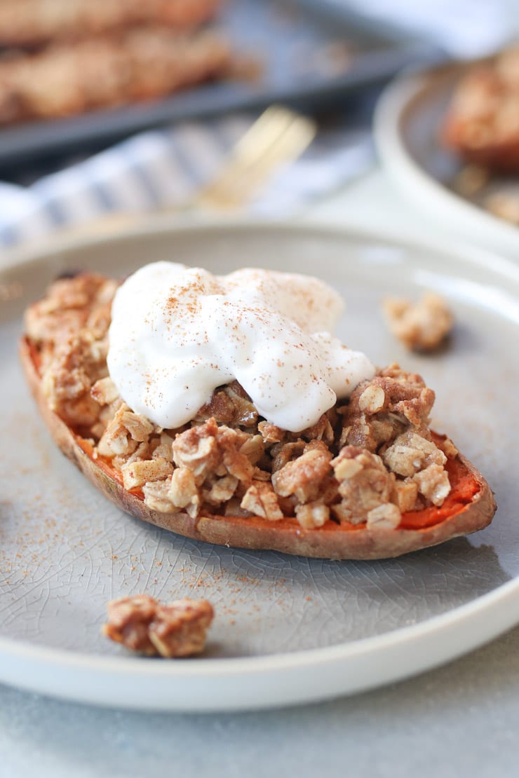 Close up of sweet potato stuffed with apple crisp topped with a vegan cream on a grey plate.