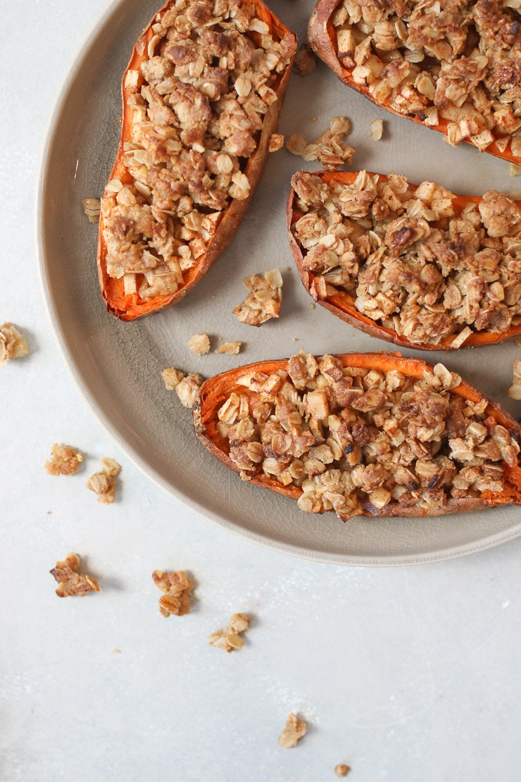 Three sweet potatoes stuffed with vegan apple crisp on a grey plate.
