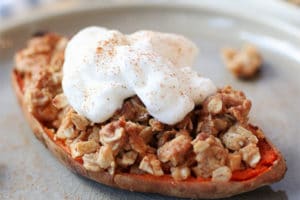 Close up of sweet potato stuffed with apple crisp topped with vegan cream on a grey plate.