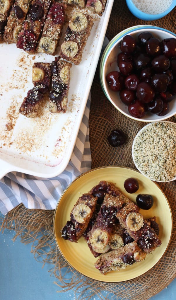 Birds eye view of a yellow plate with cherry almond baked oatmeal baby finger next to a bowl of cherries and a white casserole dish.