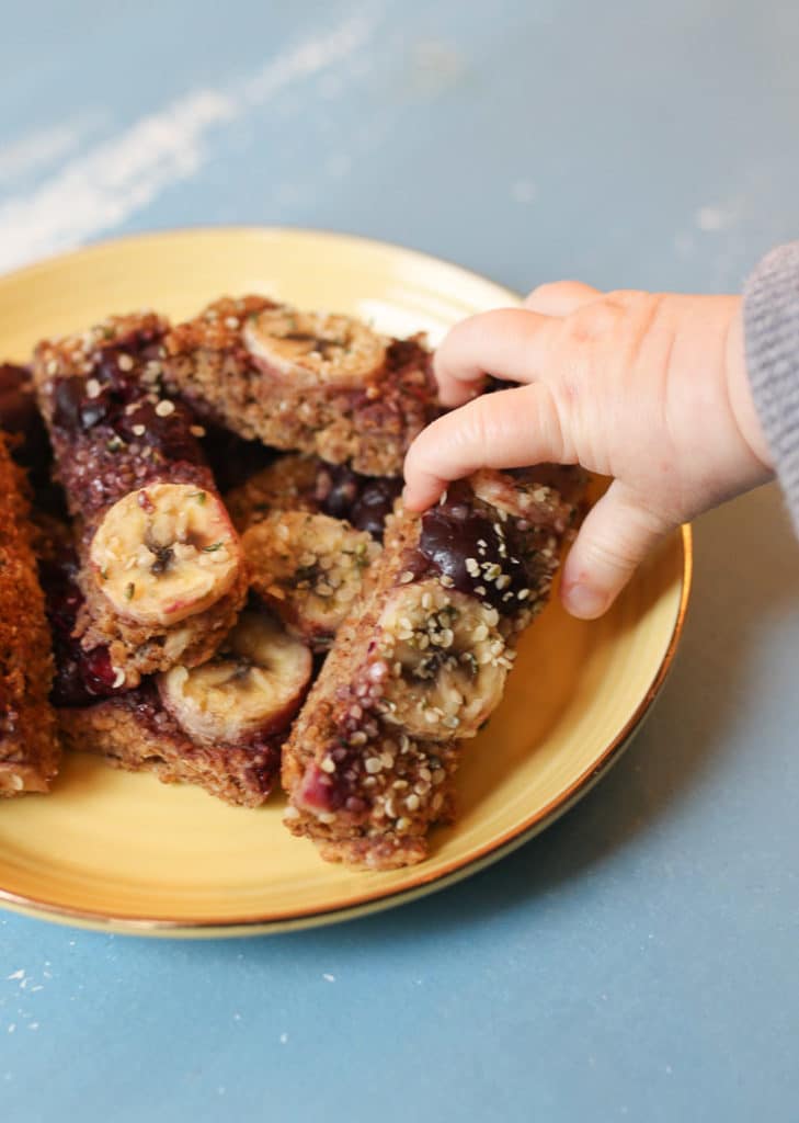 Baby grabbing a cherry almond baked oatmeal baby finger from a yellow plate.