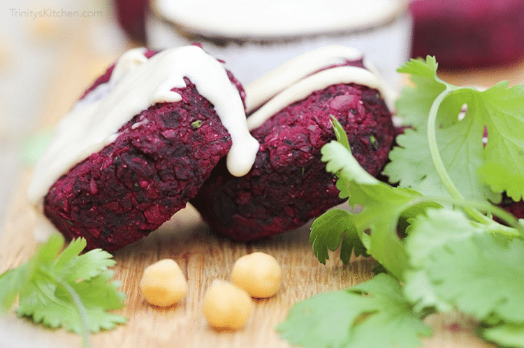 close up image of two roasted beetroot falafels garnished with herbs and tahini