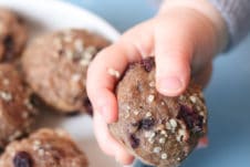 Baby hand holding mini muffin next to a white bowl filled with mini muffins.