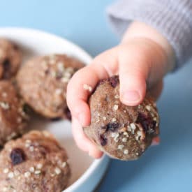 Baby hand holding mini muffin next to a white bowl filled with mini muffins.