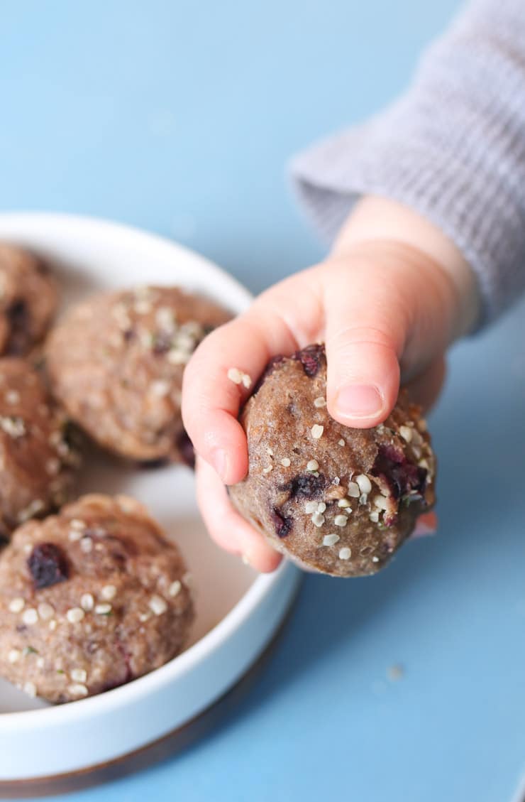 Baby hand holding mini muffin next to a white bowl filled with mini muffins.