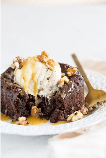 close up of vegan flourless brownie on a white plate garnished with ice cream and nuts 