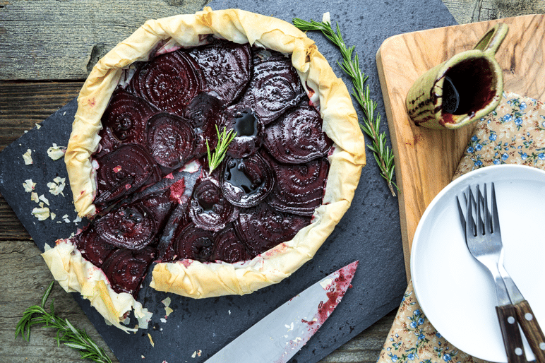 birds eye view of vegan balsamic roasted beet and rosemary cashew cheese filo tart on a black serving dish garnished with fresh herbs