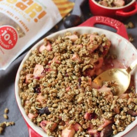 A gold spoon sitting in a red casserole dish containing granola fruit crisp.