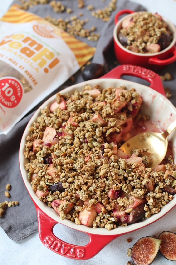 A gold spoon sitting in a red casserole dish of the best apple crisp recipe.