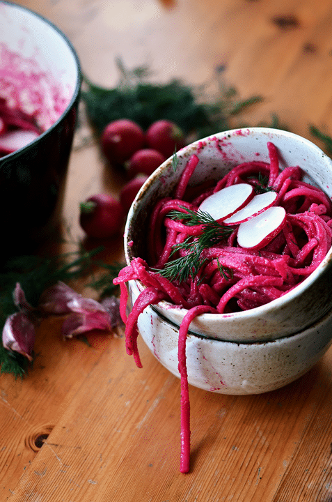 close up of vegan beetroot dill linguine in a small grey bowl garnished with radishes and herbs