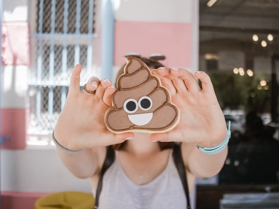 Person holding up a cookie shaped like a poop emoji.