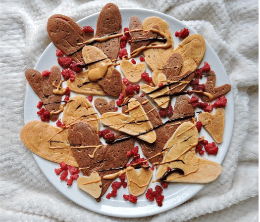 birds eye view of vegan heart shaped valentines pancakes on a white plate topped with raspberries and nut butter