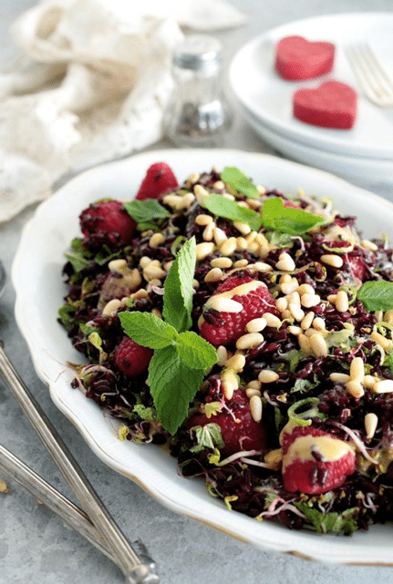 vegan black rice and raspberry salad garnished with pine nuts and fresh herbs in a large white dish