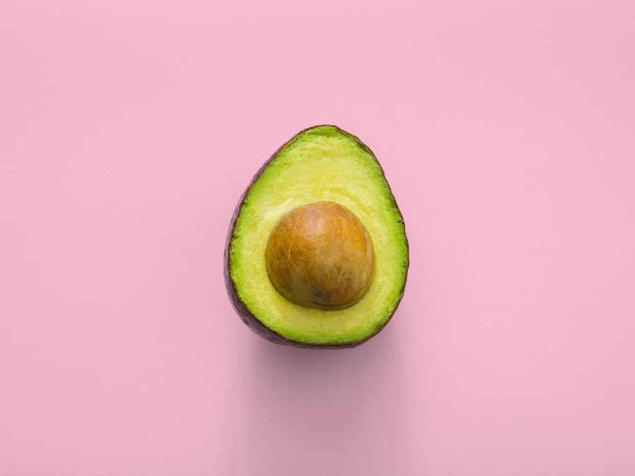 half of an avocado on a pink background