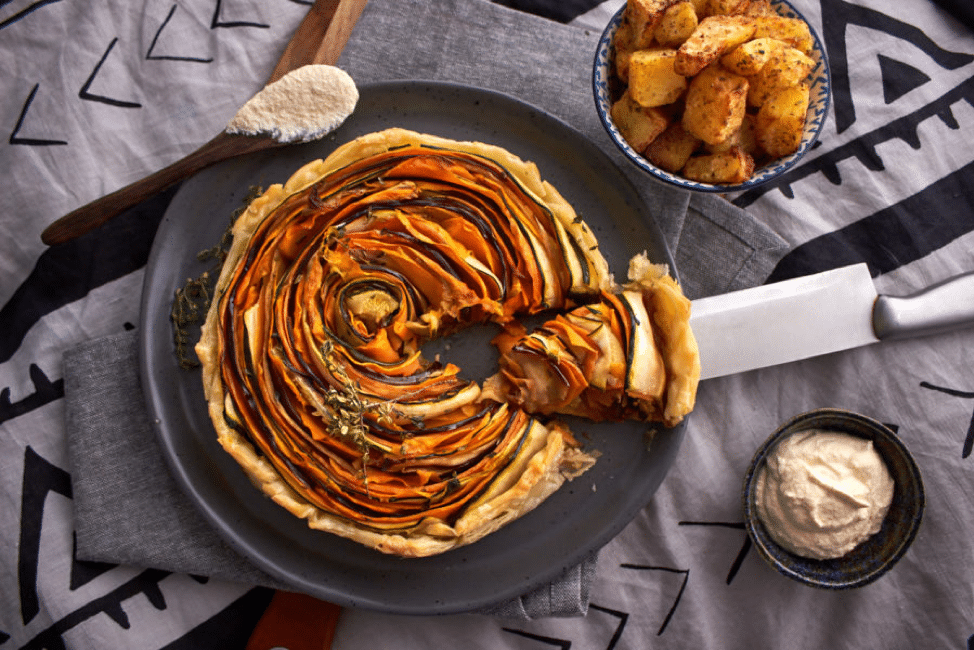 birds eye view of spiral vegetable tart on a black dish with a knife taking a slice out