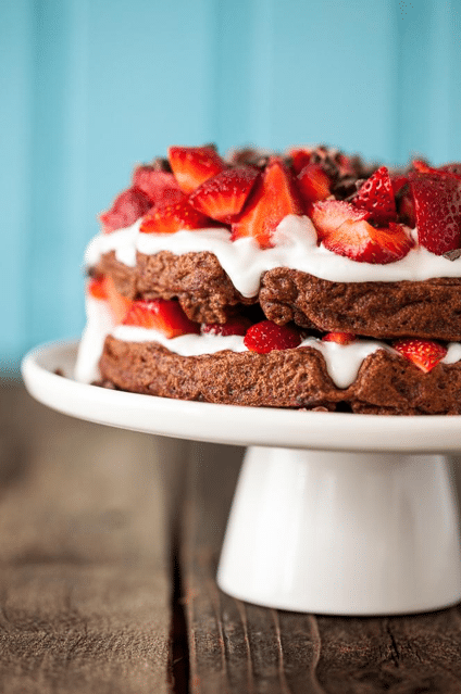 close up image of vegan chocolate strawberry shortcake waffles topped with cream and strawberries on a white dish