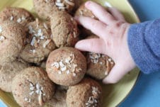 Baby hand grabbing a chickpea peanut butter baby biscuit from a yellow plate.