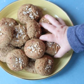 Baby hand grabbing a chickpea peanut butter baby biscuit from a yellow plate.