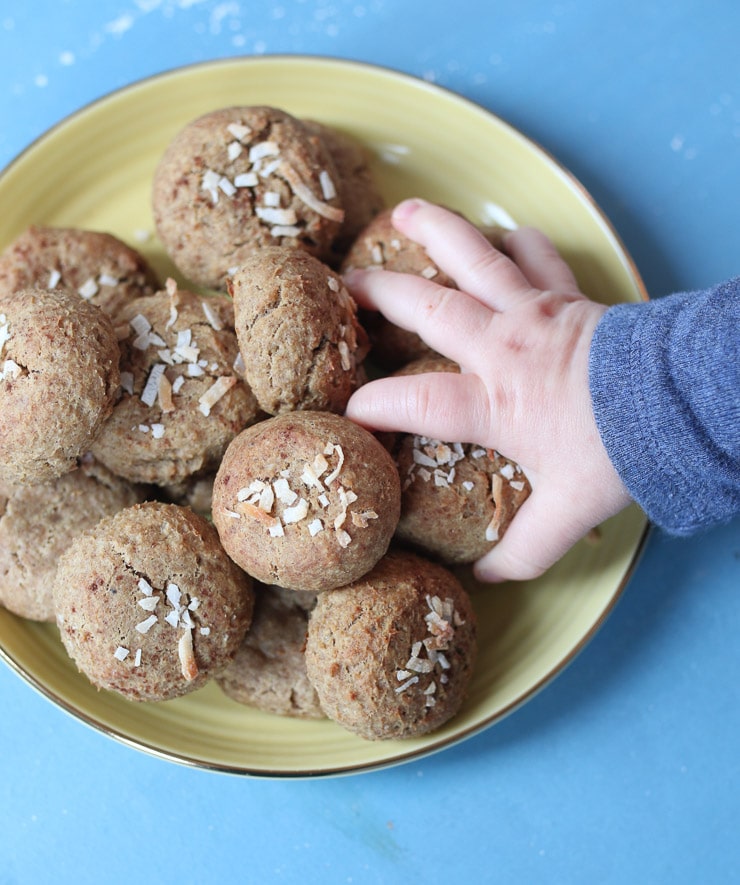 Baby hand grabbing a chickpea peanut butter baby biscuit from a yellow plate.