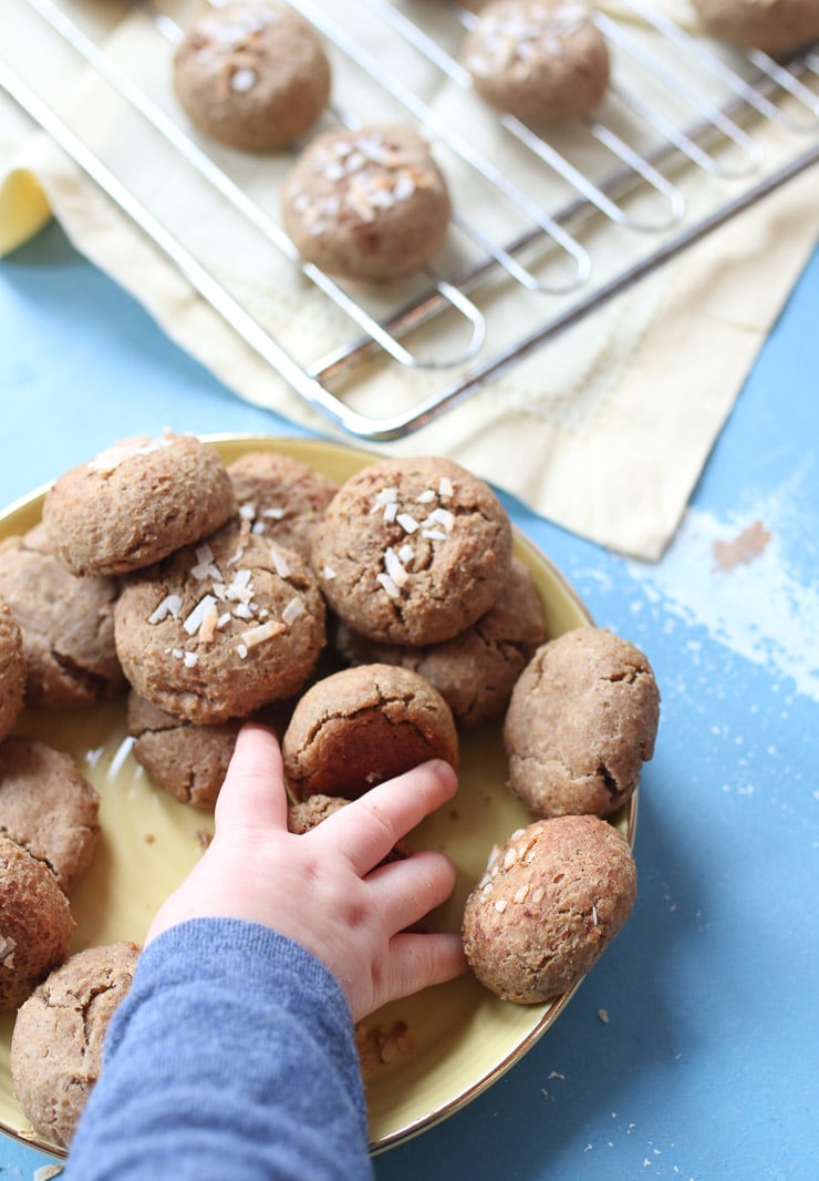 Baby hand grabbing a chickpea peanut butter baby biscuits from a yellow plate.