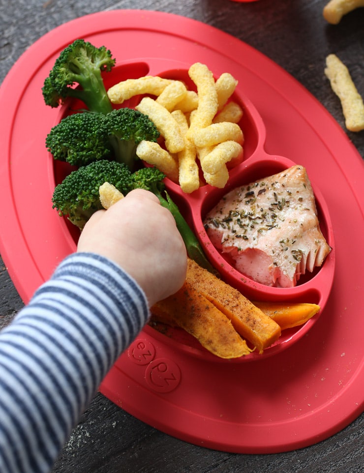 Baby grabbing at baby led weaning lunch on a red plate.