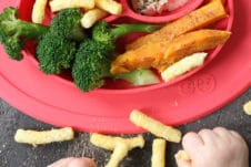 Baby playing with food next to a red plate with baby led weaning lunch.